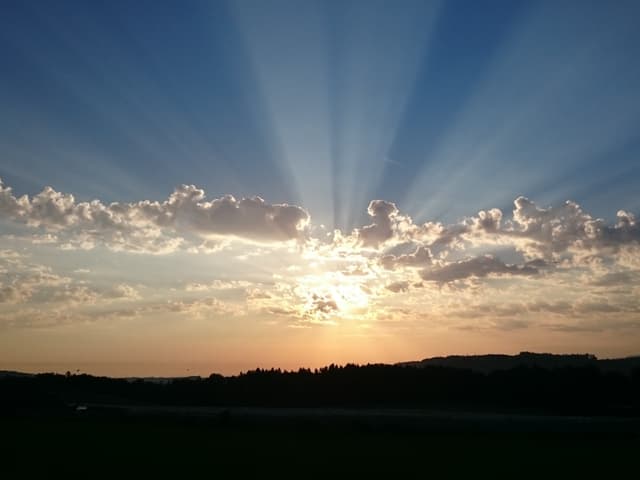 Sonnenaufgang hinter Wolken mit Morgenrot. Darüber blauer Himmel.