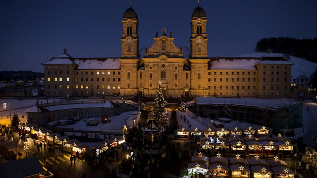 Ein grosses Kloster, davor leuchten die Lichter eines Weihnachtsmarktes. Ein grosses Kloster, davor leuchten die Lichter eines Weihnachtsmarktes.