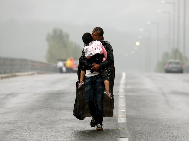 Ein syrischer Flüchtling gibt seiner Tochter einen Kuss, während er in strömendem Regen zur mazedonischen Grenze läuft.