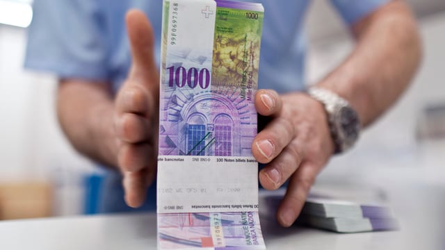 Mann hält ein Bündel Tausendernoten auf dem Tisch Mann hält ein Bündel Tausendernoten auf dem Tisch