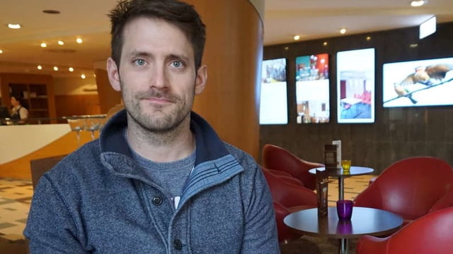 Ein Mann sitzt in einer Cafeteria und schaut in die Kamera Ein Mann sitzt in einer Cafeteria und schaut in die Kamera