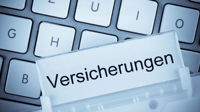 Ein Dossier, beschriftet mit «Versicherungen» liegt auf einer Computertastatur Ein Dossier, beschriftet mit «Versicherungen» liegt auf einer Computertastatur
