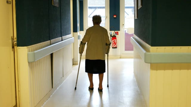 Eine Seniorin geht an Krücken den Gang entlang Eine Seniorin geht an Krücken den Gang entlang