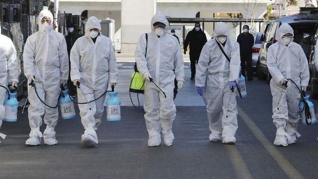 Personen in Schutzkleidung und Sprühflaschen in Daegu, Südkorea. Personen in Schutzkleidung und Sprühflaschen in Daegu, Südkorea.