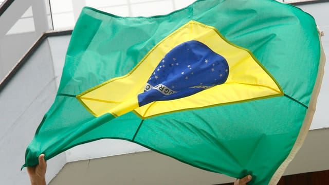 Eine Brasilienfahne wird vor einem Gebäude in die Luft gehalten Eine Brasilienfahne wird vor einem Gebäude in die Luft gehalten