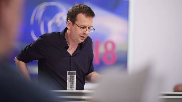 Ein Autor mit Brille liest vor, vor ihm steht ein Wasserglas. Ein Autor mit Brille liest vor, vor ihm steht ein Wasserglas.