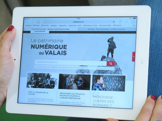 Zwei Hände halten ein iPad, darauf ist die Website Vallesiana geöffnet.