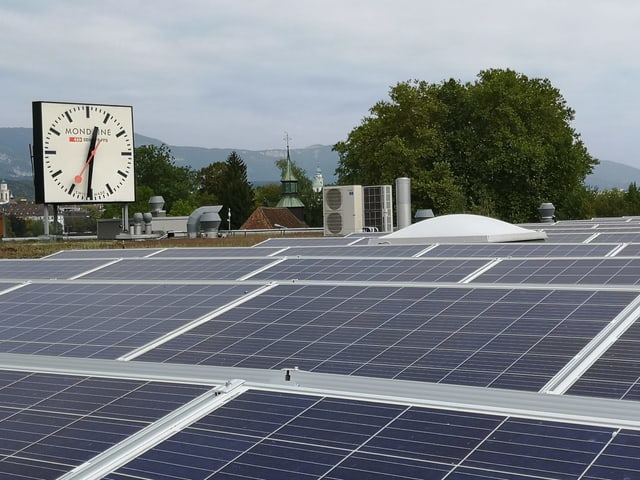 Solaranlage auf einem Flachdach. Dahinter eine grosse Uhr. Solaranlage auf einem Flachdach. Dahinter eine grosse Uhr.