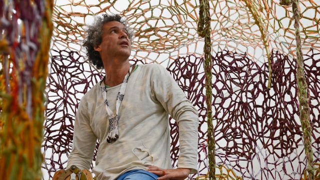 Ernesto Neto sitzt vor einem gehäkelten Netz. Ernesto Neto sitzt vor einem gehäkelten Netz.