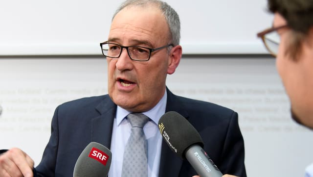 Guy Parmelin vor zwei Radiomikrofonen, rechts im Bild angeschnitten ein Journalist. Guy Parmelin vor zwei Radiomikrofonen, rechts im Bild angeschnitten ein Journalist.