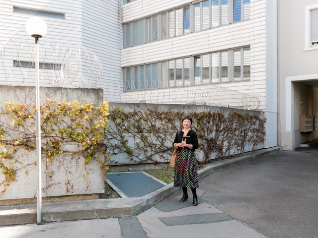 Eine Frau mit gepunktetem Rock steht vor einer Betonwand, welche mit einem Stacheldrathzaun versehen ist. Eine Frau mit gepunktetem Rock steht vor einer Betonwand, welche mit einem Stacheldrathzaun versehen ist.