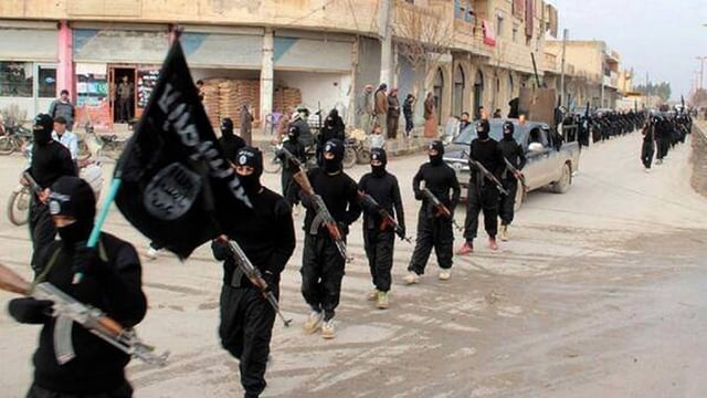 Schwarz vermummte Männer mit Gewehren marschieren durch eine syrische Stadt. Schwarz vermummte Männer mit Gewehren marschieren durch eine syrische Stadt.