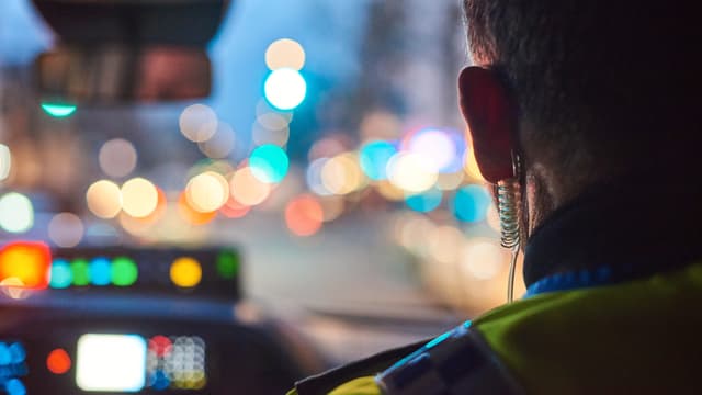 Bild von hinten in einem Auto nach vorne. Man sieht den Kopf eines Polizisten und die abendlichen Lichter in der Frontscheibe. Bild von hinten in einem Auto nach vorne. Man sieht den Kopf eines Polizisten und die abendlichen Lichter in der Frontscheibe.