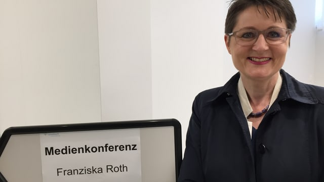 Franziska Roth neben einem Wegweiser zu ihrer 100-Tage-Medienkonferenz