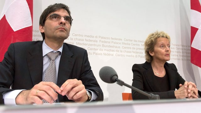 Brunetti sitzt links, Widmer-Schlumpf rechts, dahinter Schweizer Fahnen. Brunetti sitzt links, Widmer-Schlumpf rechts, dahinter Schweizer Fahnen.