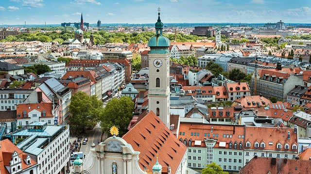 Blick von einer Anhöhe auf die Stadt München mit vielen Ziegeldächern und einem Kirchenturm. Blick von einer Anhöhe auf die Stadt München mit vielen Ziegeldächern und einem Kirchenturm.