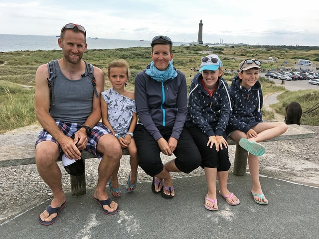 Familie Bernhard sitzt draussen auf einer Steinbank, im Hintergrund ist ein Parkplatz sowie die Nordsee zu sehen. Familie Bernhard sitzt draussen auf einer Steinbank, im Hintergrund ist ein Parkplatz sowie die Nordsee zu sehen.