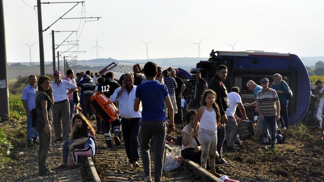Zahlreiche Menschen neben umgestürzten Waggons. Zahlreiche Menschen neben umgestürzten Waggons.