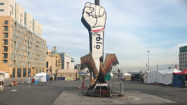 Revolution statt Weihnachten auf dem Märtyrerplatz in Beirut: Gereckte Faust statt Weihnachtsbaum. Davor ein Phönix aus den Stäben von zertrümmerten und abgebrannten Zelten. Immer wieder greifen Schlägertrupps die Demonstranten an und zerstören ihre Zelte. Revolution statt Weihnachten auf dem Märtyrerplatz in Beirut: Gereckte Faust statt Weihnachtsbaum. Davor ein Phönix aus den Stäben von zertrümmerten und abgebrannten Zelten. Immer wieder greifen Schlägertrupps die Demonstranten an und zerstören ihre Zelte.