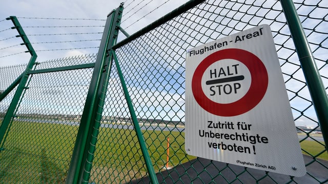 Ein Schild hängt an einem Zaun, darauf steht: "Halt - Stop". Dahinter ist eine Landebahn am Zürcher Flughafen. Ein Schild hängt an einem Zaun, darauf steht: "Halt - Stop". Dahinter ist eine Landebahn am Zürcher Flughafen.