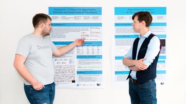 Zwei Männer stehen vor einem Plakat, das die Details zu den Forschungsergebnissen auflistet. Zwei Männer stehen vor einem Plakat, das die Details zu den Forschungsergebnissen auflistet.