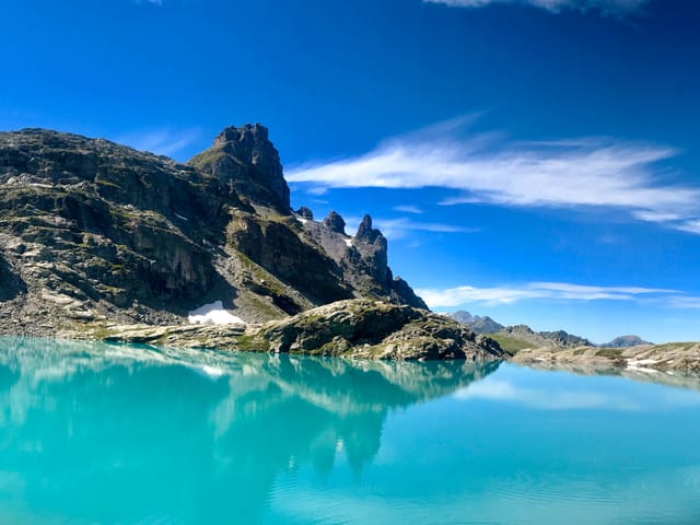 Blauer Bergsee. Dahinter Berge, Schneereste und blauer Himmel.