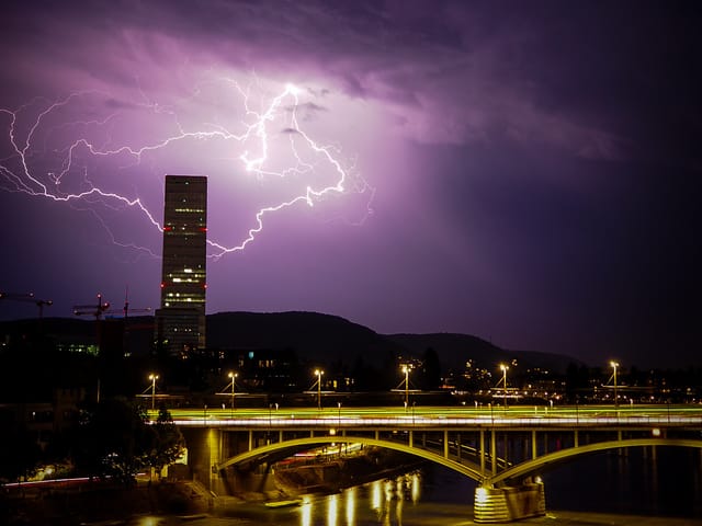 Beleuchtete Brücke und Blitze am Himmel.