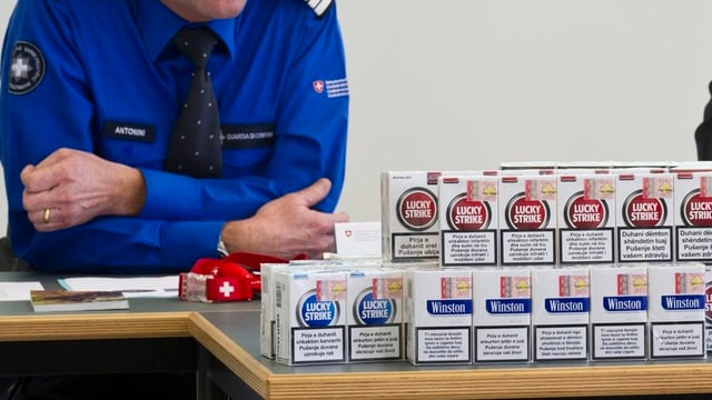 Uniformierter sitzt an einem Tisch voller Zigaretten-Päckli. Uniformierter sitzt an einem Tisch voller Zigaretten-Päckli.