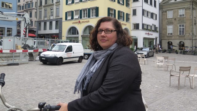 Eine Frau im Halbporträt steht mit ihrem Velo auf dem Münsterhof Eine Frau im Halbporträt steht mit ihrem Velo auf dem Münsterhof