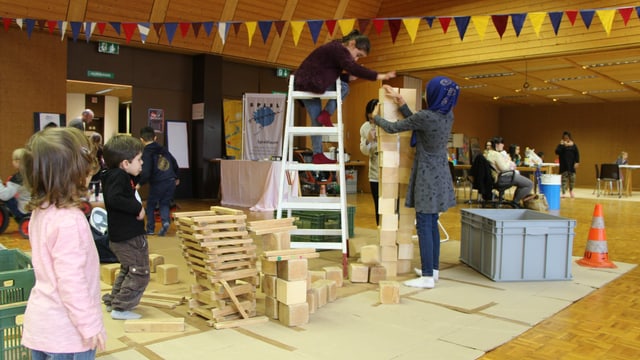 Kinder bauen mit Holzklötzen einen Turm. Ein Kind auf Leiter. Kinder bauen mit Holzklötzen einen Turm. Ein Kind auf Leiter.