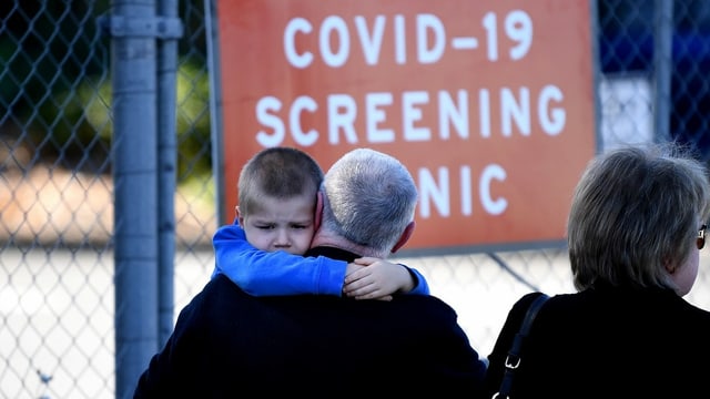 Mann mit Kind vor Schild: Covid-19-Screening-Center Mann mit Kind vor Schild: Covid-19-Screening-Center