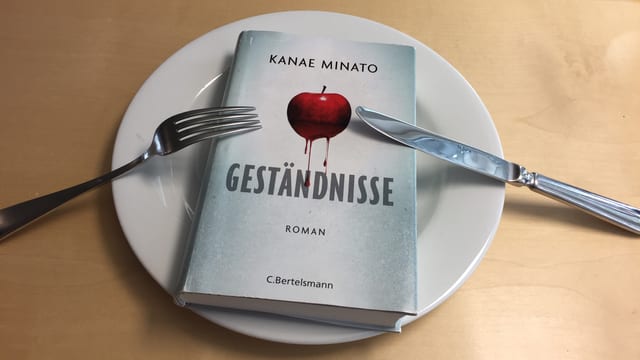 Der Thriller «Geständnisse» von Kanae Minato liegt auf einem Teller, das Besteck liegt darauf aufgestützt und impliziert ich will noch mehr Der Thriller «Geständnisse» von Kanae Minato liegt auf einem Teller, das Besteck liegt darauf aufgestützt und impliziert ich will noch mehr