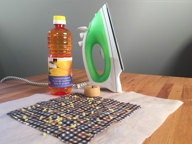 Ein Bügeleisen, Öl, Bienenwachs und ein Tuch liegen auf einem Tisch.
