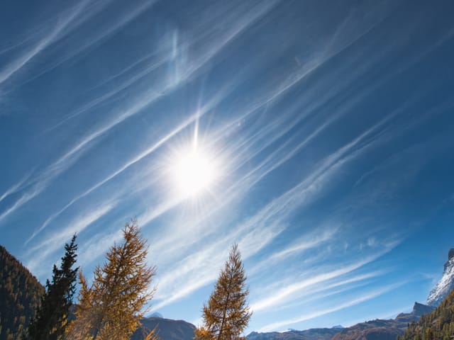 Blauer Himmel mit weissen Strichen und Sonne.