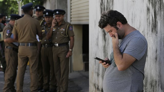 Ein Tourist schaut auf sein Smartphone, im Hintergrund Männer in Uniform. Ein Tourist schaut auf sein Smartphone, im Hintergrund Männer in Uniform.