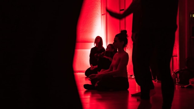 Menschen sitzen in einem rot beleuchteten Raum am Boden Menschen sitzen in einem rot beleuchteten Raum am Boden