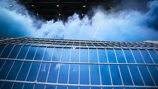 Ein Stadiongitter: dahinter sind Fans und blauer Rauch. Ein Stadiongitter: dahinter sind Fans und blauer Rauch.