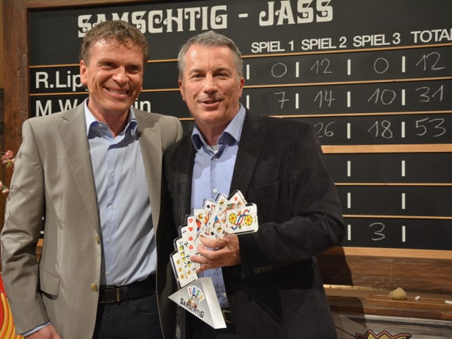 Dani Müller mit Gewinner Reto Lipp mit Pokal in der Hand vor der Jasstafel