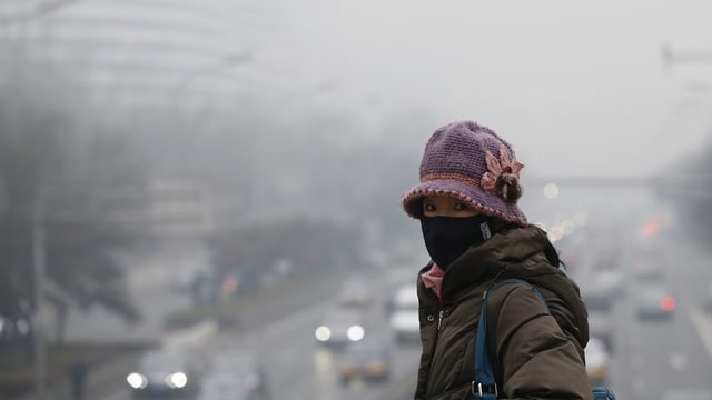 Chinesische Frau mit Mundschutz vor Stadt mit Smog Chinesische Frau mit Mundschutz vor Stadt mit Smog