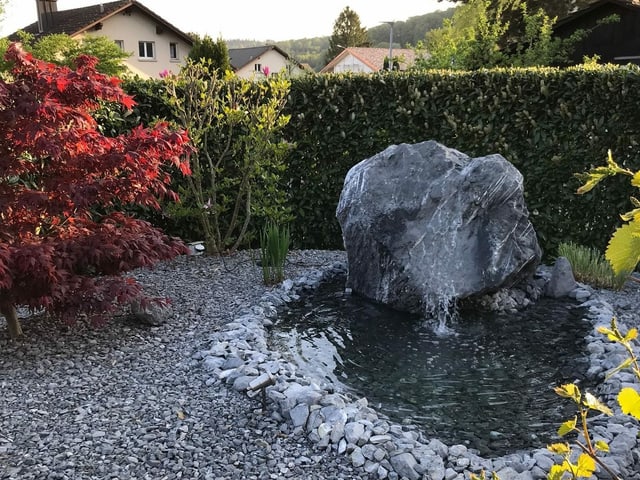 Brunnen mit gtrossem Stein in einem Steingarten.