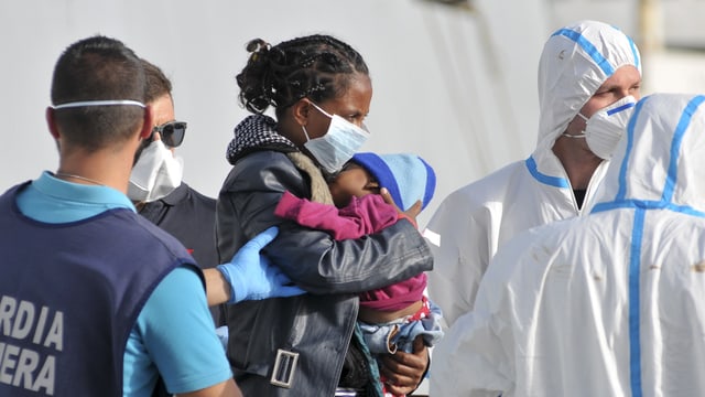 Eine Flüchtlingsfrau mit Kleinkind geht auf Sizilien an Land. Eine Flüchtlingsfrau mit Kleinkind geht auf Sizilien an Land.