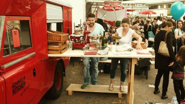 Foodtruck mit ausgezogenem Tisch und zwei Personen, die ihn dekorieren. Foodtruck mit ausgezogenem Tisch und zwei Personen, die ihn dekorieren.