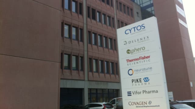 Vor einem Gebäude steht eine Säule, auf der die Namen verschiedener Firmen aufgelistet sind.