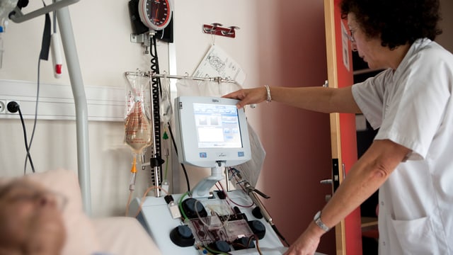 Eine Ärztin macht sich an einem Screen zu schaffen, im Vordergrund liegt ein Patient im Bett. Eine Ärztin macht sich an einem Screen zu schaffen, im Vordergrund liegt ein Patient im Bett.