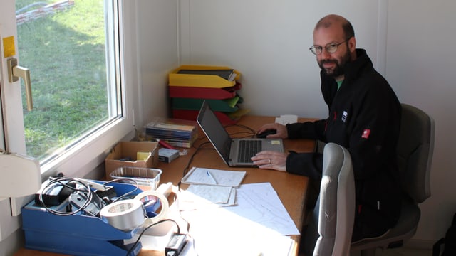 Mann sitzt mit Laptop an Tisch Mann sitzt mit Laptop an Tisch
