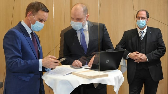 Drei Männer mit Anzug und Maske vor Laptop