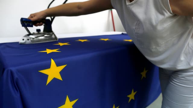 Eine Näherin streicht mit einem Bügeleisen über eine EU-Flagge. Eine Näherin streicht mit einem Bügeleisen über eine EU-Flagge.