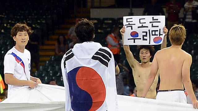 Koreas Park Jong Woo hält umringt von Teamkollegen seine umstrittene Botschaft hoch. Koreas Park Jong Woo hält umringt von Teamkollegen seine umstrittene Botschaft hoch.