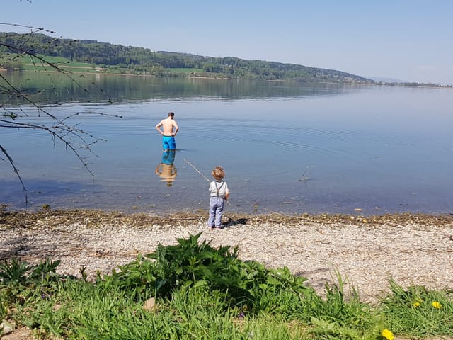 See, am Ufer ein kleines Kind, im knietiefen Wasser ein Mann in Badehose.