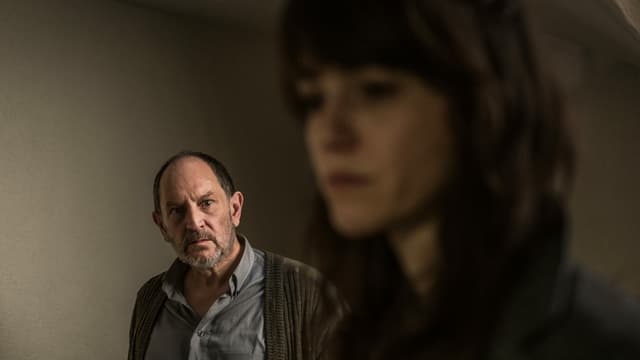 Ein Mann schaut mit ernstem Blick. Im Vordergruind ist unscharf eine Frau zu erkennen Ein Mann schaut mit ernstem Blick. Im Vordergruind ist unscharf eine Frau zu erkennen
